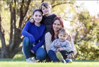 Rochelle and her 3 children sitting on the grass in front of a tree.